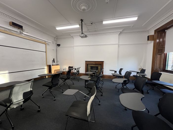 Flat floored teaching room with rows of tablet chairs, whiteboard, projector, lectern, and PC.