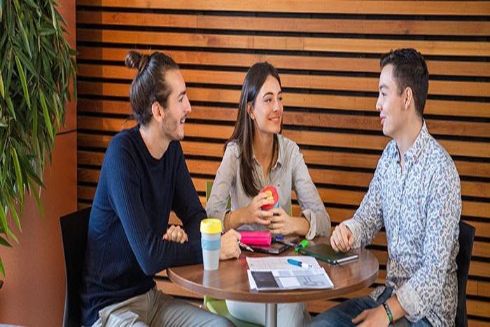 Three students talking at a table in the University Library. 