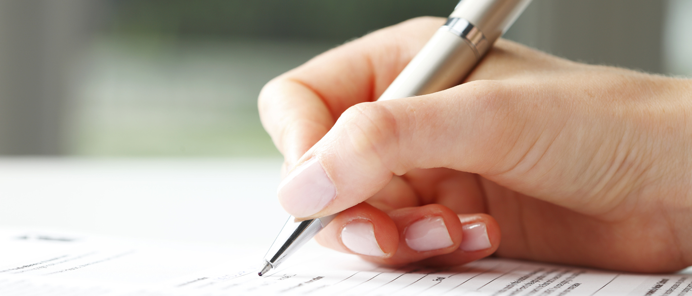 Photo of a person's hand holding a pen and completing an application form
